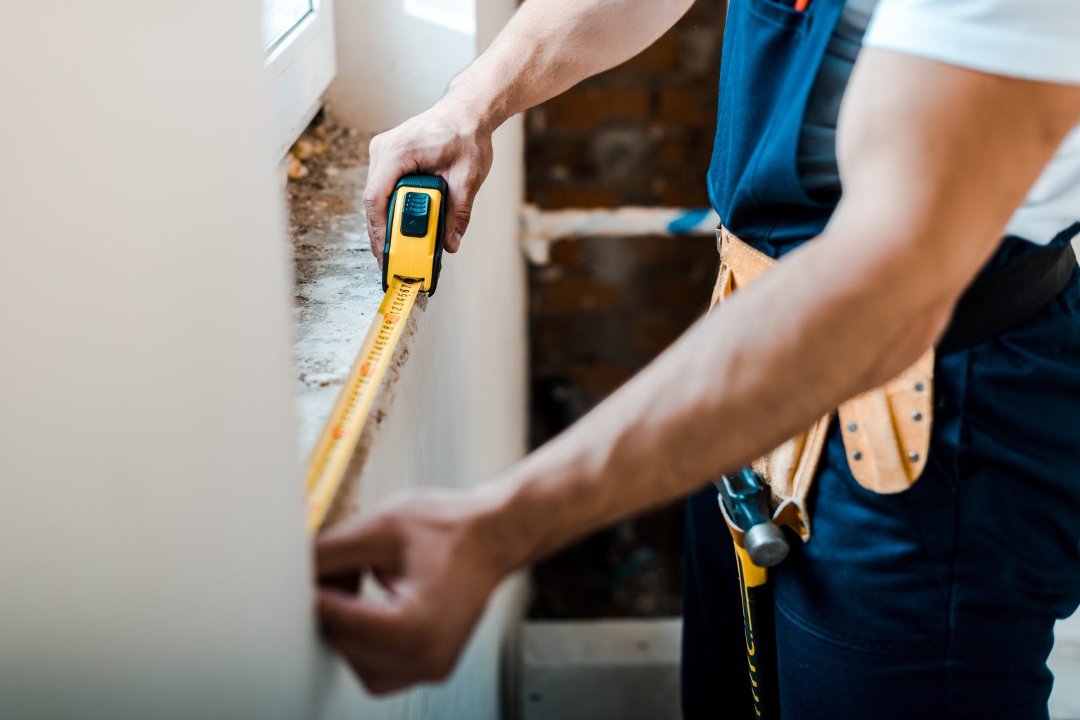 Handyman measuring a wall with a tape measure during a repair